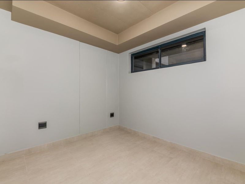 A clean, empty room featuring neutral tiled flooring, a recessed ceiling detail, and a high-set horizontal window providing natural light.