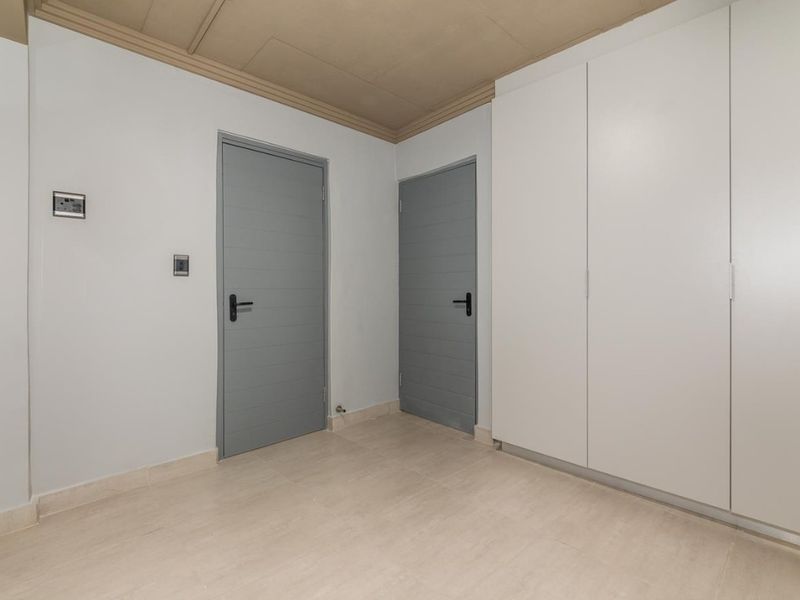 A clean, empty bedroom featuring built-in white cabinetry, neutral tiled flooring, and two grey interior doors.