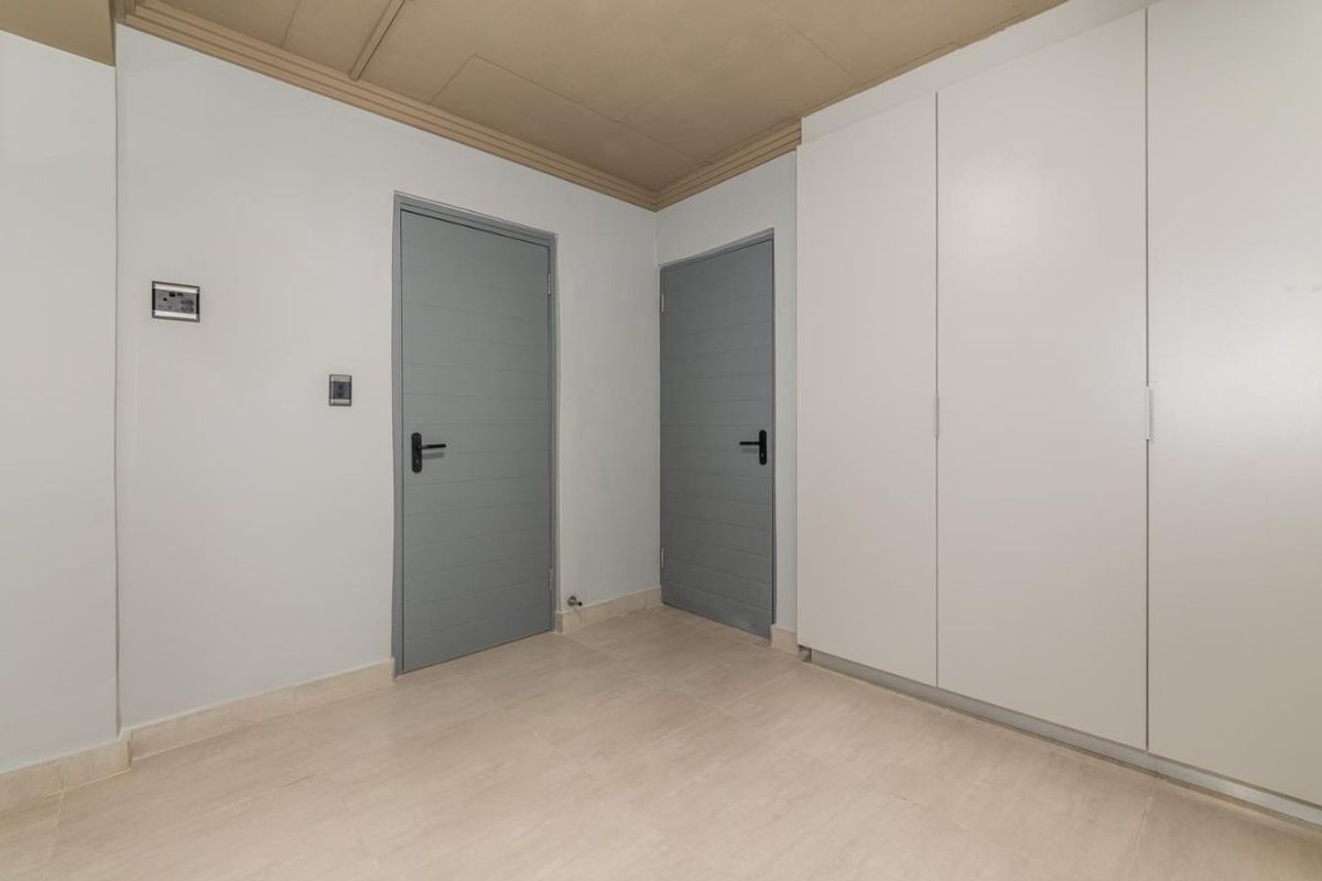 A clean, empty bedroom featuring built-in white cabinetry, neutral tiled flooring, and two grey interior doors.