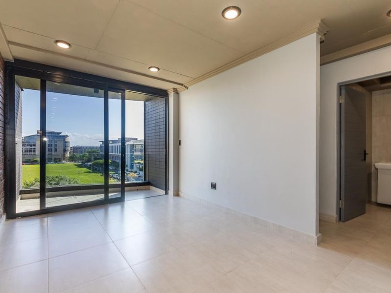 A bright, open-plan living area featuring a striking exposed brick wall, large sliding glass doors leading to a balcony, and an adjoining bathroom.