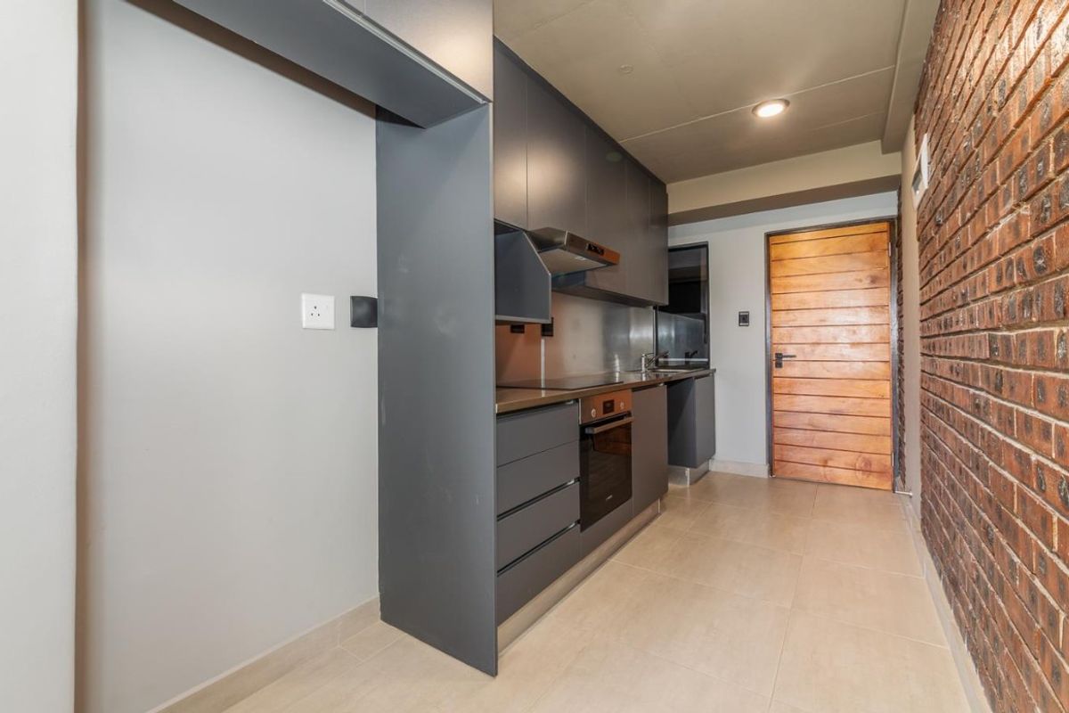 Modern galley-style kitchen featuring dark grey cabinetry, built-in oven, extractor fan, and a striking exposed brick feature wall.
