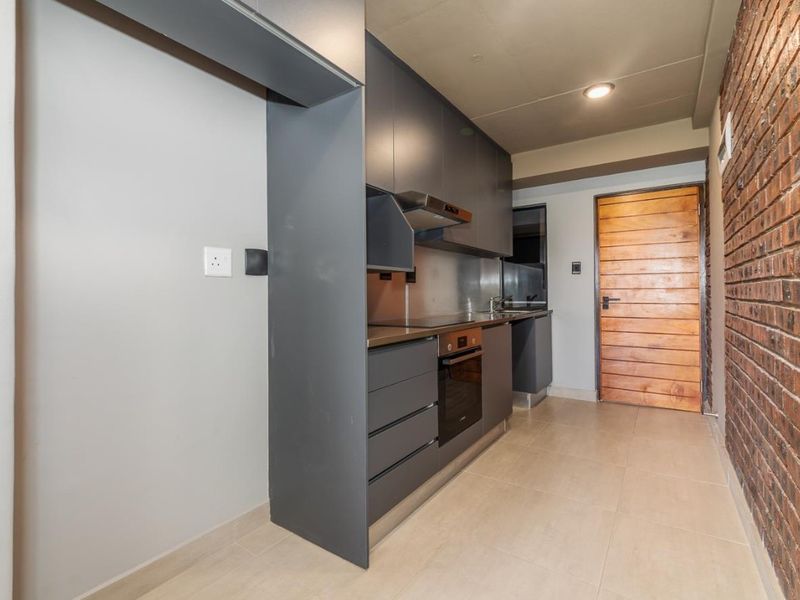 Modern galley-style kitchen featuring dark grey cabinetry, built-in oven, extractor fan, and a striking exposed brick feature wall.