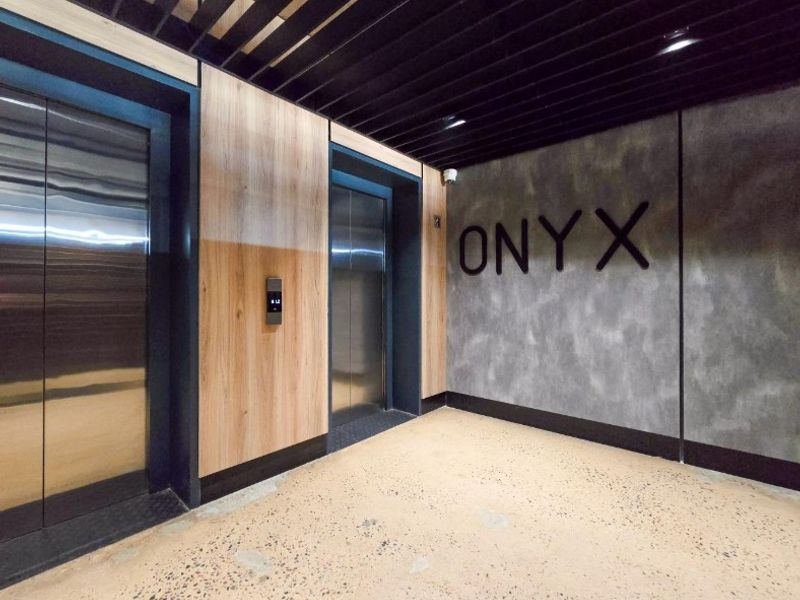 Modern apartment building elevator lobby featuring polished concrete flooring, wood-paneled walls, and contemporary black ceiling slats.