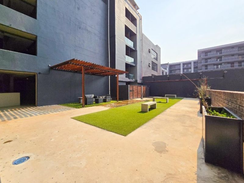A communal outdoor patio area featuring a wooden pergola, artificial turf sections, and built-in concrete seating benches within an apartment complex.
