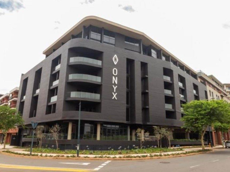 A modern multi-story apartment building exterior featuring a dark facade, glass balconies, and prominent building signage on a corner street location.