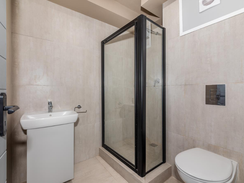 Modern bathroom featuring a glass-enclosed shower, wall-mounted toilet with concealed cistern, and a pedestal basin with neutral floor-to-ceiling tiling.