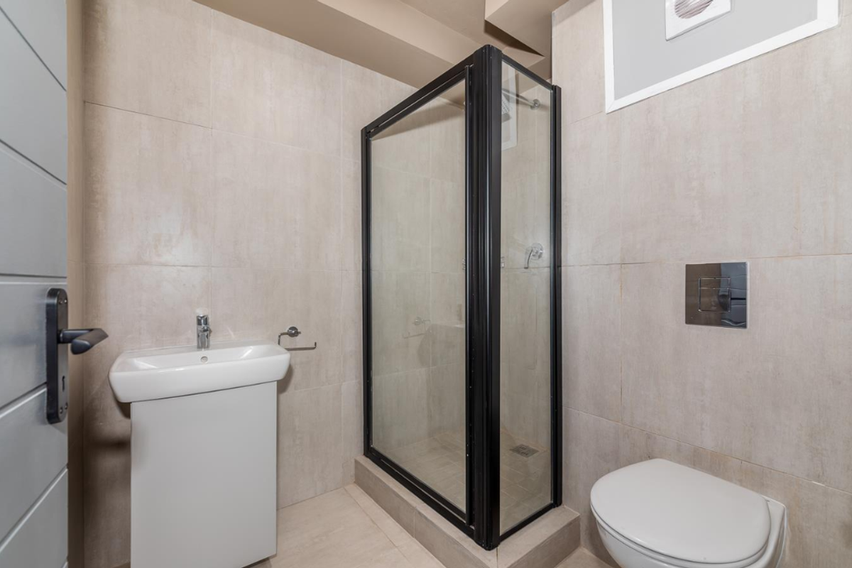 Modern bathroom featuring a glass-enclosed shower, wall-mounted toilet with concealed cistern, and a pedestal basin with neutral floor-to-ceiling tiling.