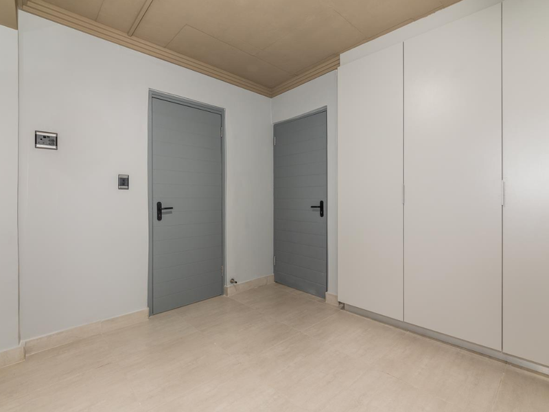 A clean, neutral hallway featuring tiled flooring, built-in white cabinetry, and two grey interior doors.