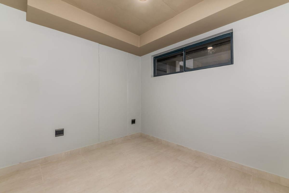 A clean, empty room featuring neutral tiled flooring, a high-level horizontal window, and a recessed ceiling detail.