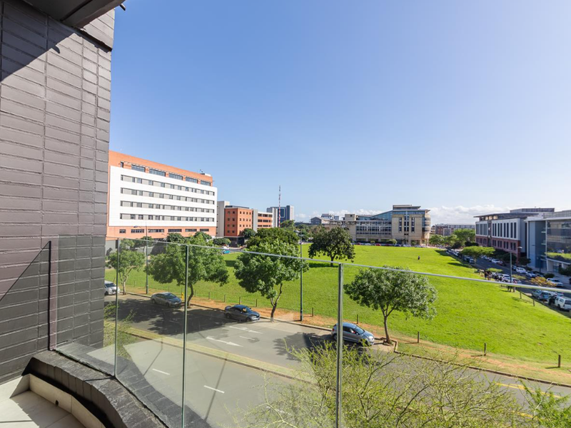 A view from a balcony overlooking a green park area and surrounding urban buildings.