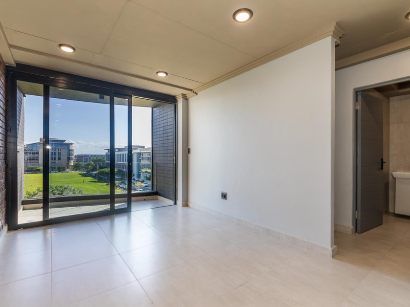 A bright, open-plan living area featuring a striking exposed brick wall, large sliding glass doors leading to a balcony, and an adjacent bathroom.