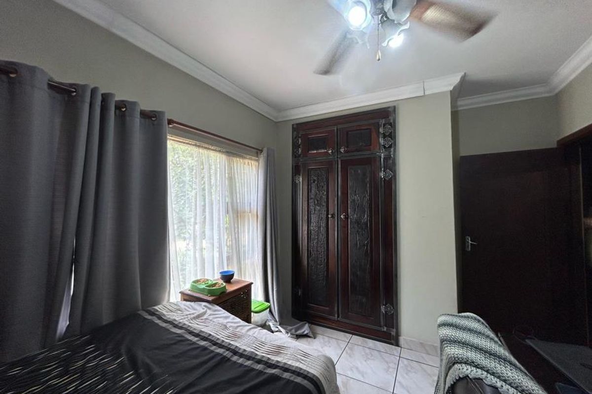 A bedroom featuring tiled flooring, a built-in dark wood wardrobe, and a ceiling fan, offering a functional space with neutral wall tones.