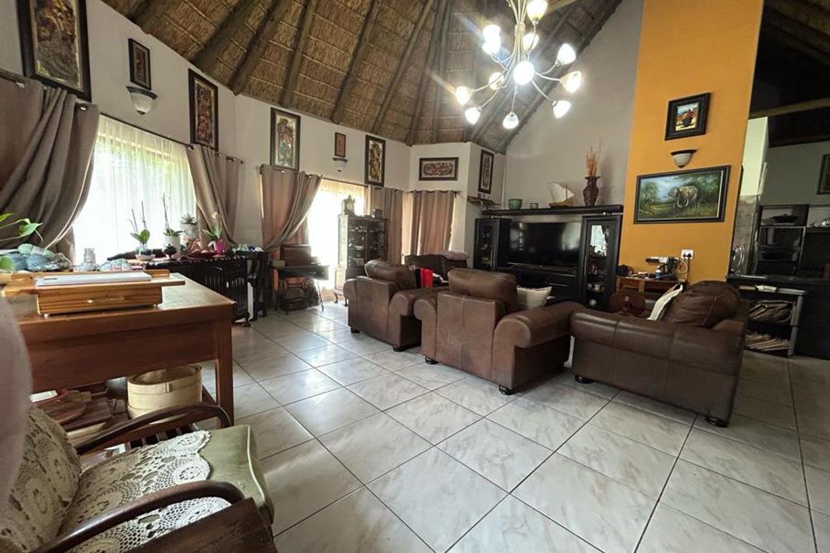 Spacious living area featuring a high vaulted thatched ceiling, tiled flooring, and a prominent feature wall, creating a warm and rustic atmosphere.