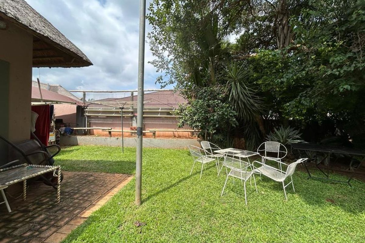 A rear garden area featuring a paved patio section, lawn, and established perimeter trees, providing a private outdoor space.