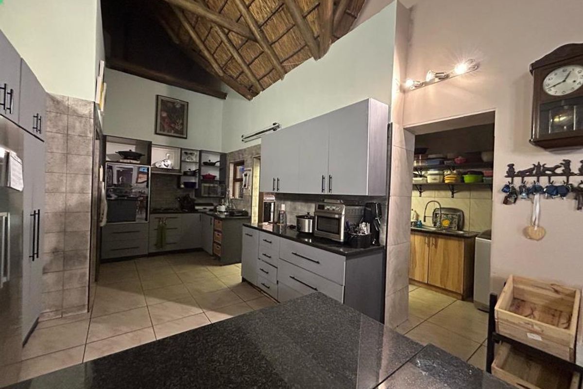 Spacious kitchen featuring modern grey cabinetry, granite countertops, and a high vaulted thatched ceiling, with an adjoining scullery area for additional storage and prep.