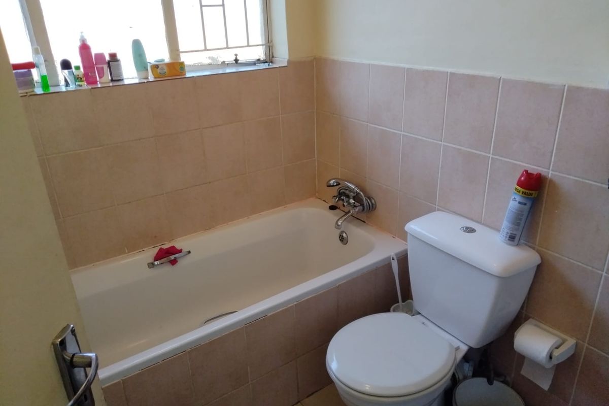 A functional bathroom featuring a standard bathtub with chrome mixer tap, a white ceramic toilet, and neutral wall tiling.