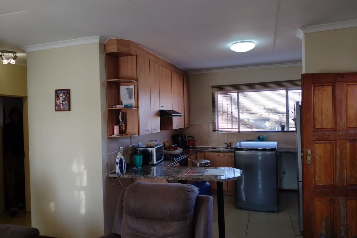 A functional kitchen featuring wooden cabinetry, a breakfast bar, tiled splashbacks, and a window with blinds, integrated into an open-plan living space.