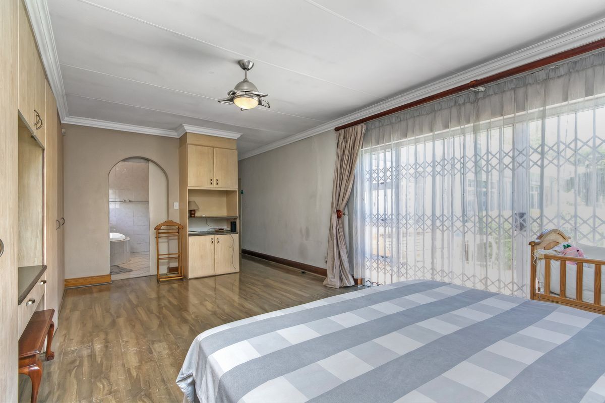 Spacious bedroom featuring built-in cabinetry, laminate flooring, and direct access to an en-suite bathroom through an arched doorway.