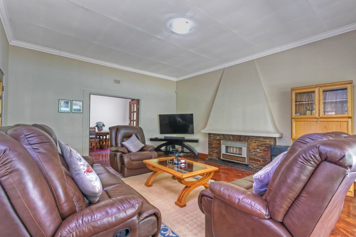 A comfortable living room featuring a prominent built-in fireplace with stone detailing and classic parquet flooring, offering a warm and inviting atmosphere.