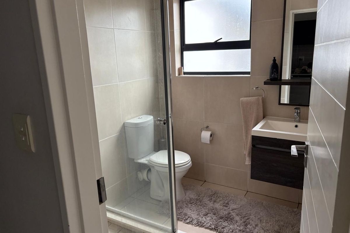 A modern bathroom featuring a glass-enclosed shower, wall-mounted vanity with basin, and neutral tiled finishes.