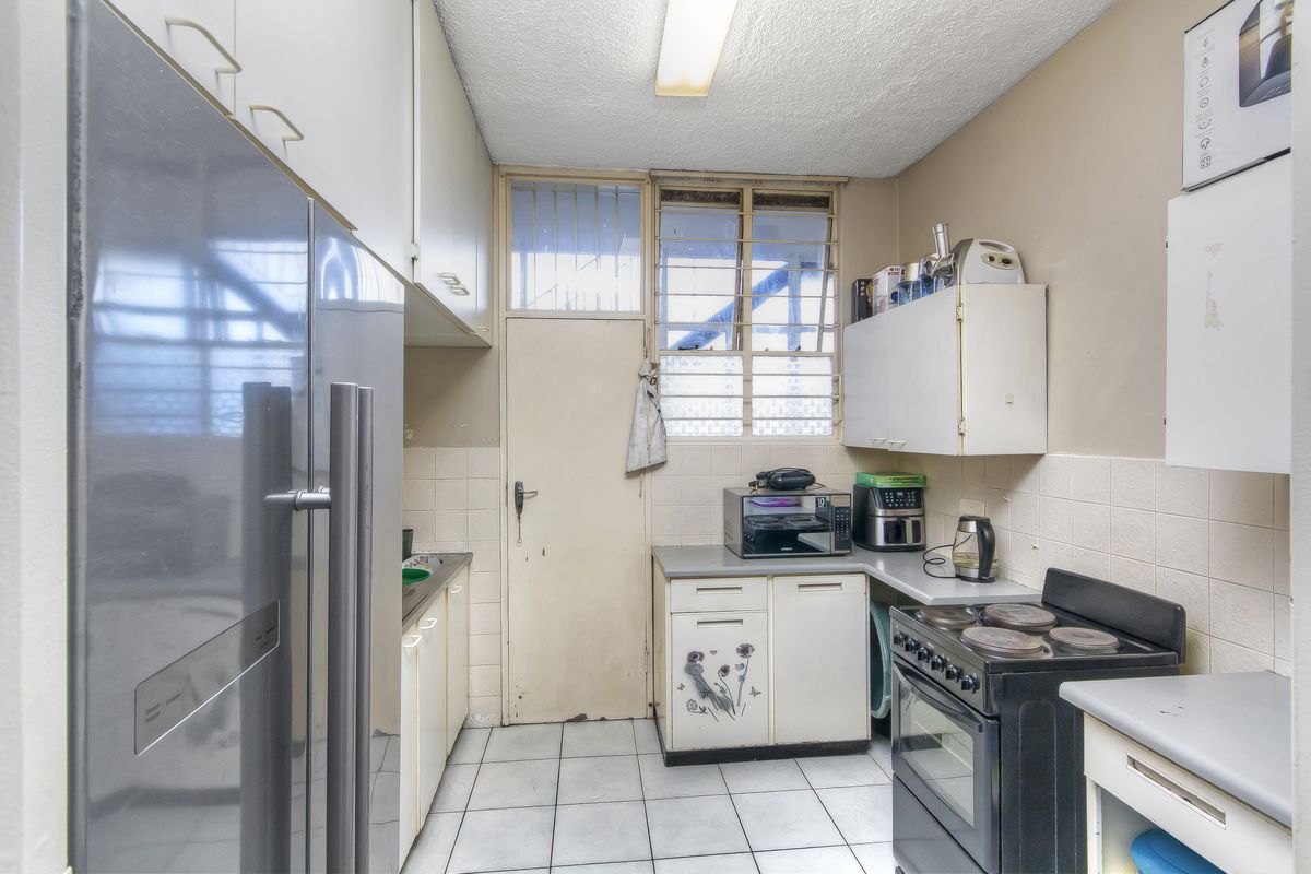 A compact, functional kitchen featuring tiled flooring, built-in cabinetry, a freestanding stove, and a rear access door with security bars.