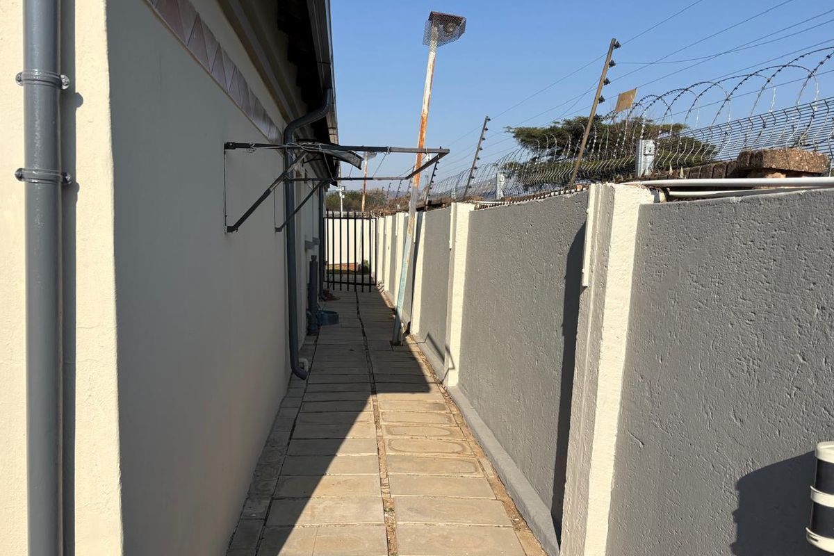 A narrow side passage featuring paved flooring, a perimeter wall with electric fencing, and a wall-mounted drying rack.