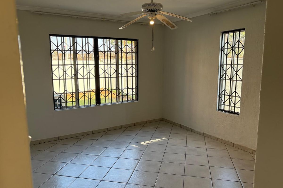 A bright, empty living room featuring tiled flooring, a ceiling fan, and security bars on the windows.