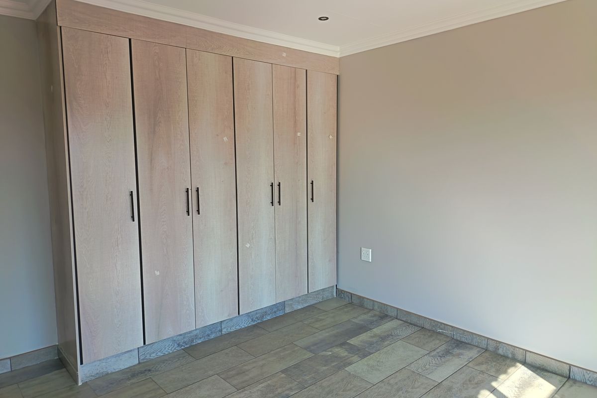 A bedroom featuring built-in wooden cabinetry with modern handles and tiled flooring.