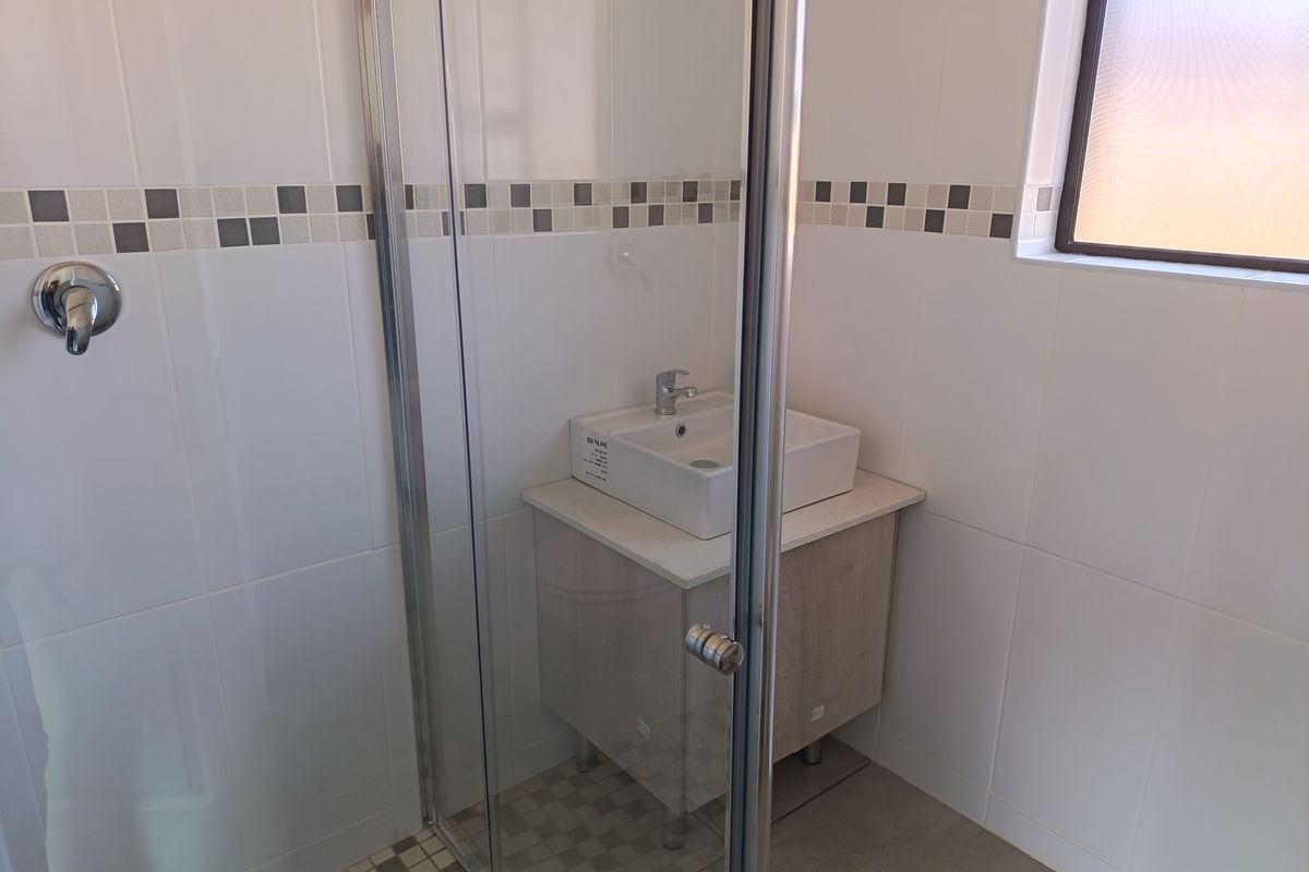 A modern bathroom featuring a glass-enclosed shower, a contemporary vanity with a vessel sink, and neutral wall tiling with a decorative mosaic border.