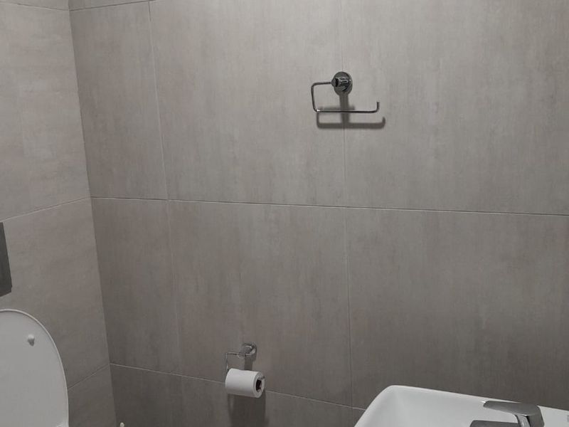 A modern bathroom featuring neutral wall tiles, a wall-mounted toilet, and a contemporary basin with a chrome mixer tap.