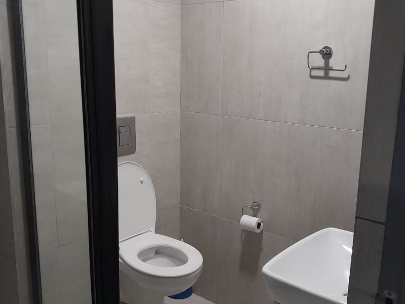 A modern bathroom featuring a wall-mounted toilet, a vanity basin, and a glass-enclosed shower with neutral floor-to-ceiling tiling.