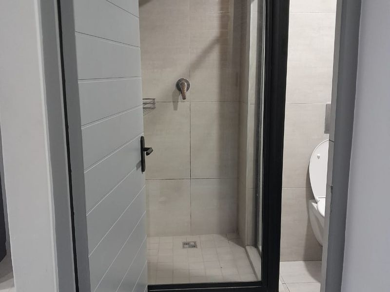 A modern bathroom featuring a walk-in shower with a black frame, tiled walls, and a wall-mounted toilet.