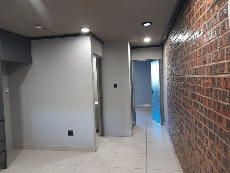 Interior hallway featuring a prominent exposed brick feature wall, neutral tiled flooring, recessed downlighting, and access to adjacent rooms.