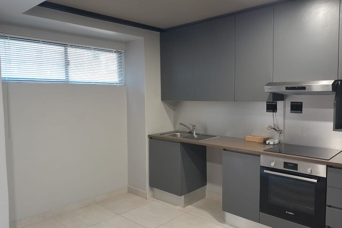 Modern kitchen featuring sleek grey cabinetry, integrated stainless steel oven, electric cooktop, extractor fan, and a stainless steel sink with tiled flooring.