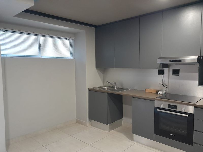 Modern kitchen featuring sleek grey cabinetry, integrated stainless steel oven, electric cooktop, extractor fan, and a stainless steel sink with tiled flooring.