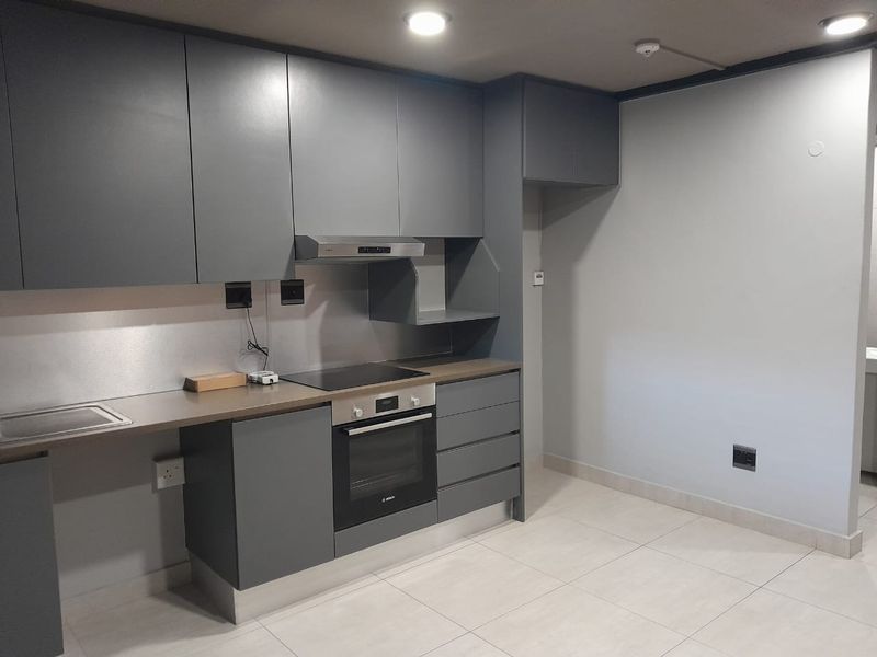 Modern kitchen featuring sleek grey cabinetry, integrated oven, electric cooktop, stainless steel extractor fan, and tiled flooring.