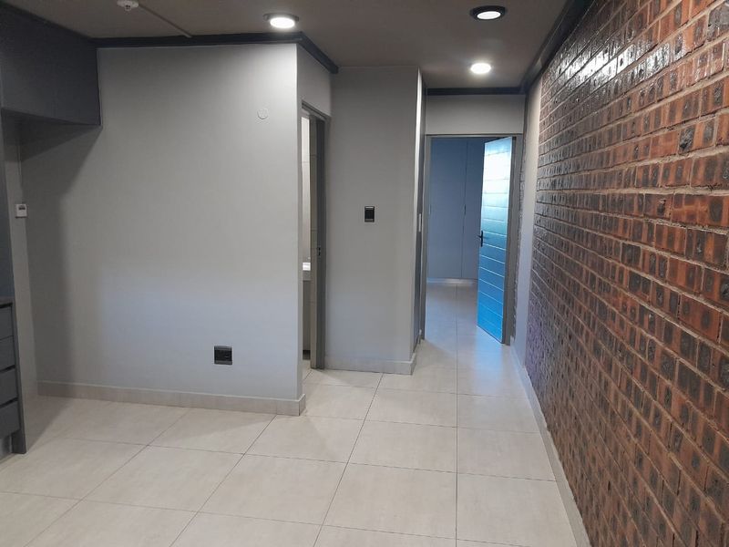 A modern interior hallway featuring a striking exposed brick feature wall, neutral tiled flooring, and recessed ceiling lighting leading to adjacent rooms.