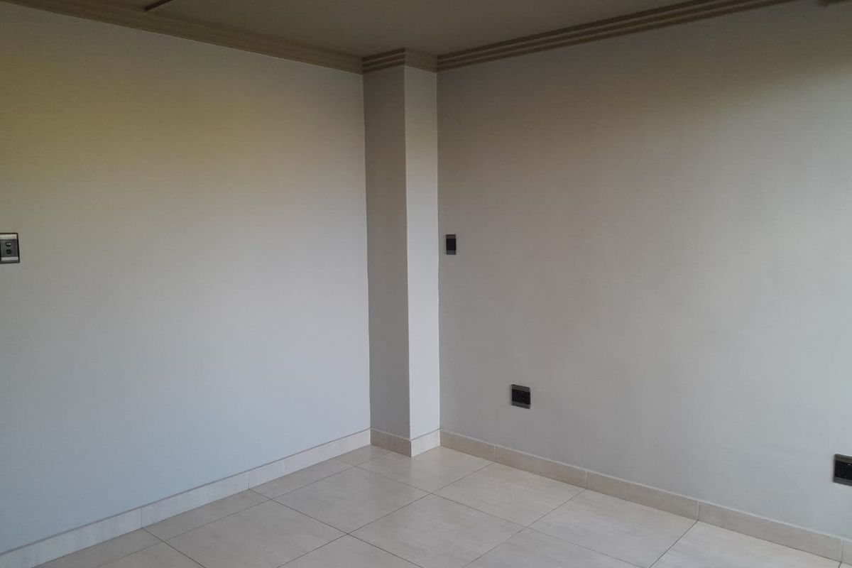 A clean, empty interior space featuring neutral tiled flooring, painted walls, and crown molding, suitable for a living or bedroom area.