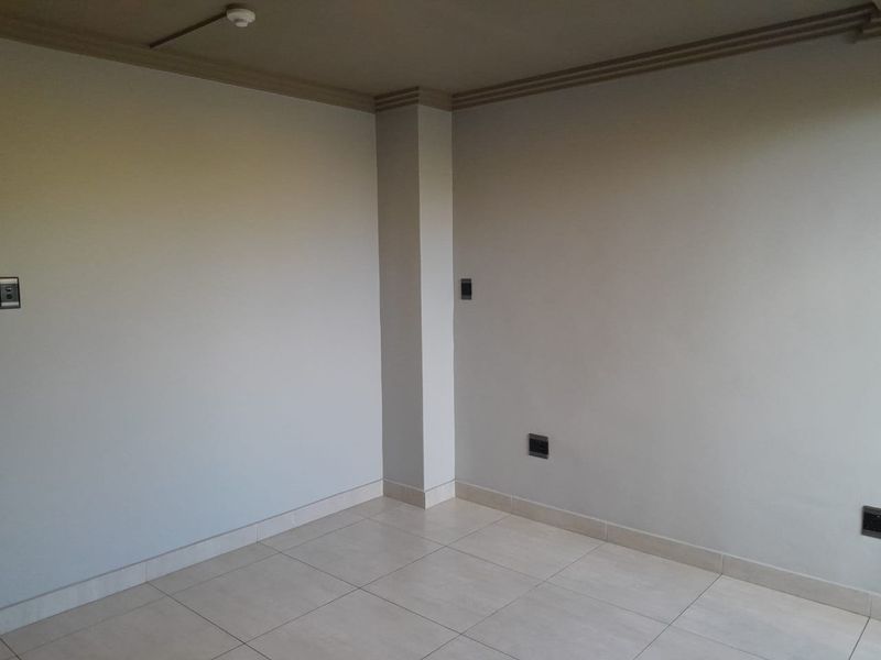A clean, empty interior space featuring neutral tiled flooring, painted walls, and crown molding, suitable for a living or bedroom area.