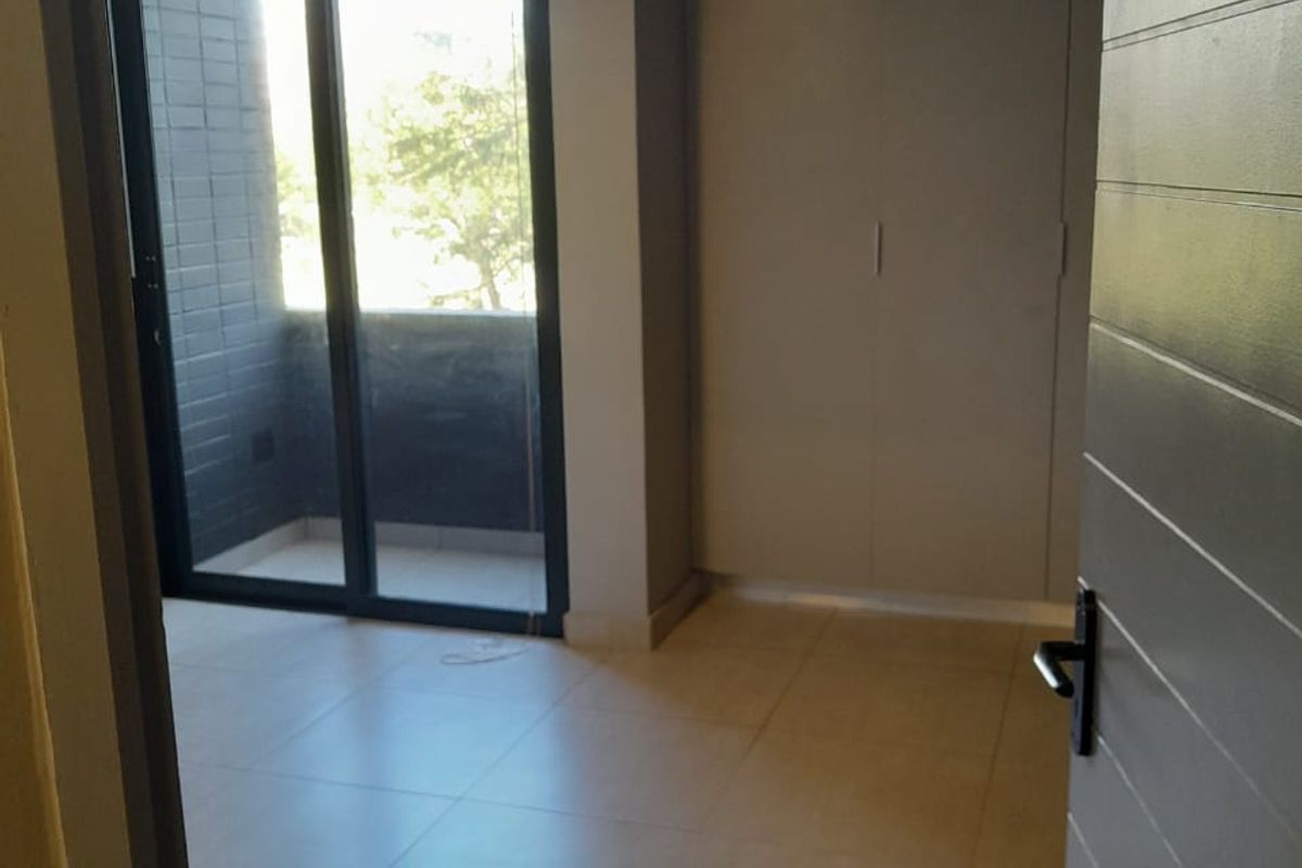 A bright, empty bedroom featuring neutral floor tiles, built-in cupboards, and sliding glass doors leading to a private balcony.