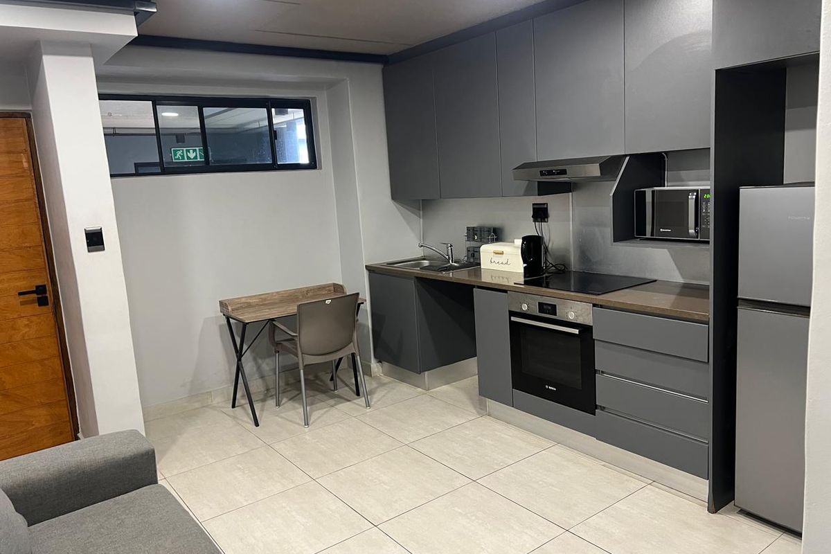 Modern open-plan kitchen featuring sleek grey cabinetry, integrated oven, hob, extractor fan, and built-in microwave, complemented by neutral floor tiling.