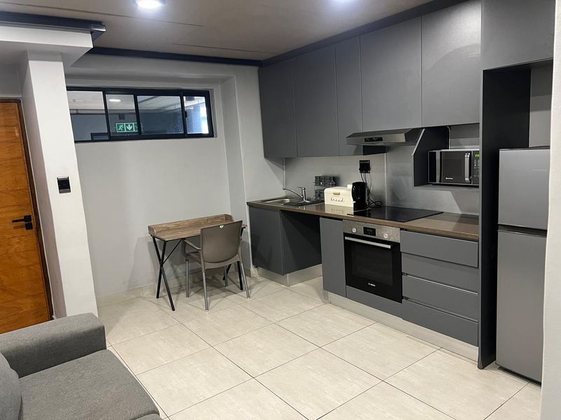 Modern open-plan kitchen featuring sleek grey cabinetry, integrated oven, hob, extractor fan, and built-in microwave, complemented by neutral floor tiling.