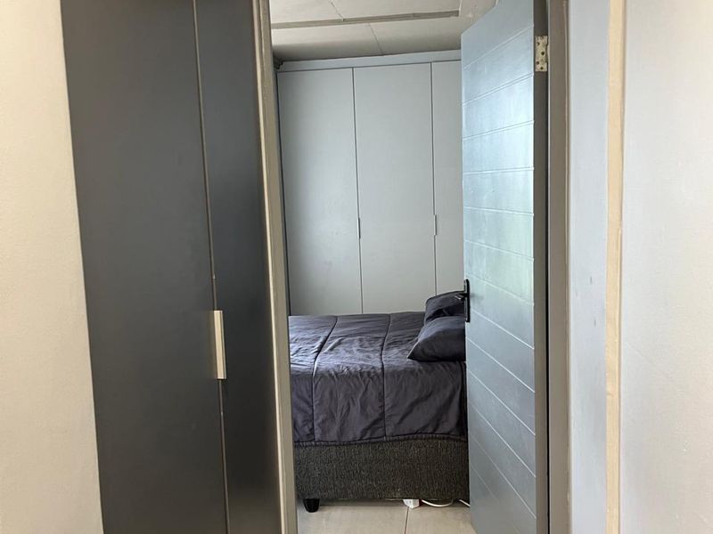 A view from a hallway into a bedroom featuring built-in cupboards, tiled flooring, and a modern grey interior door.