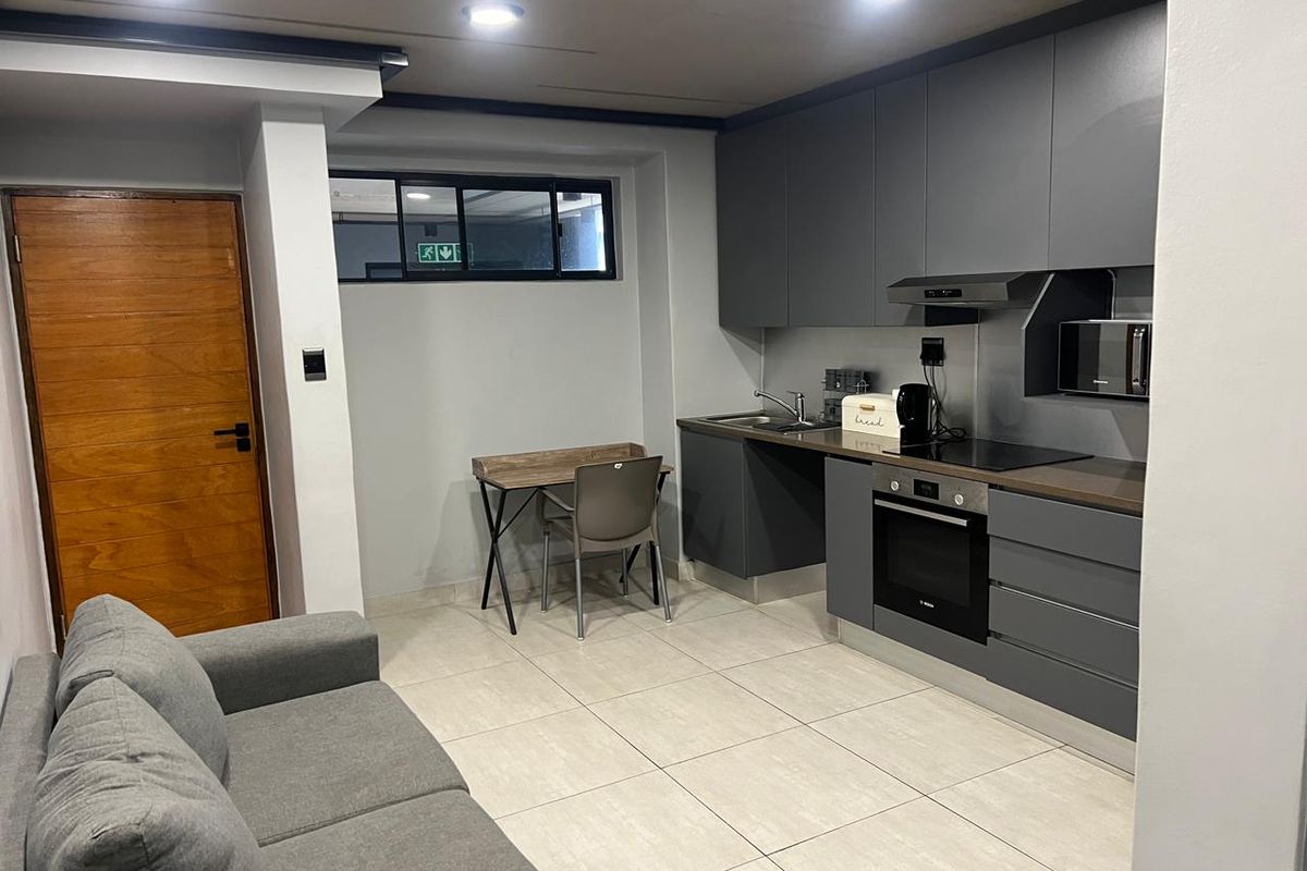 Modern open-plan kitchen featuring sleek grey cabinetry, integrated oven, hob, and extractor fan, seamlessly flowing into the living area with tiled flooring.