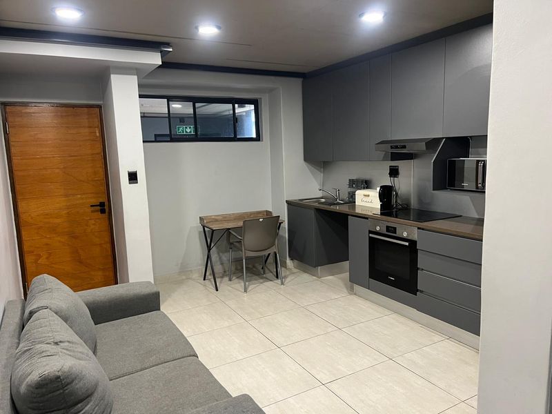 Modern open-plan kitchen featuring sleek grey cabinetry, integrated oven, hob, and extractor fan, seamlessly flowing into the living area with tiled flooring.