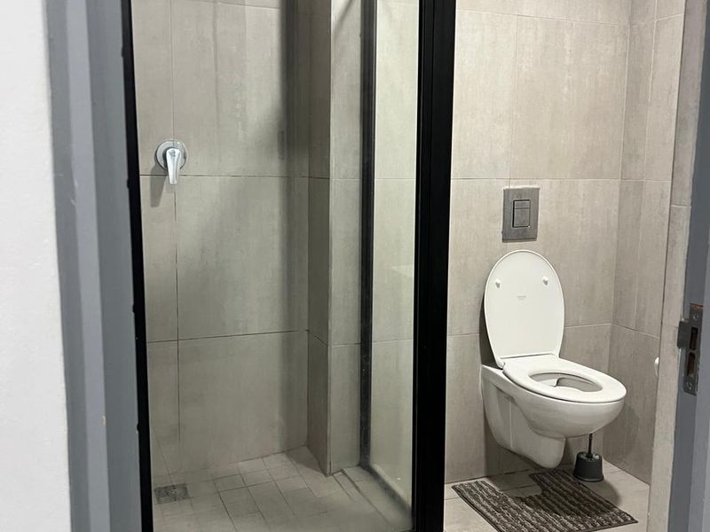 Modern bathroom featuring a walk-in shower with a black frame, wall-mounted toilet, and neutral floor-to-ceiling tiling.