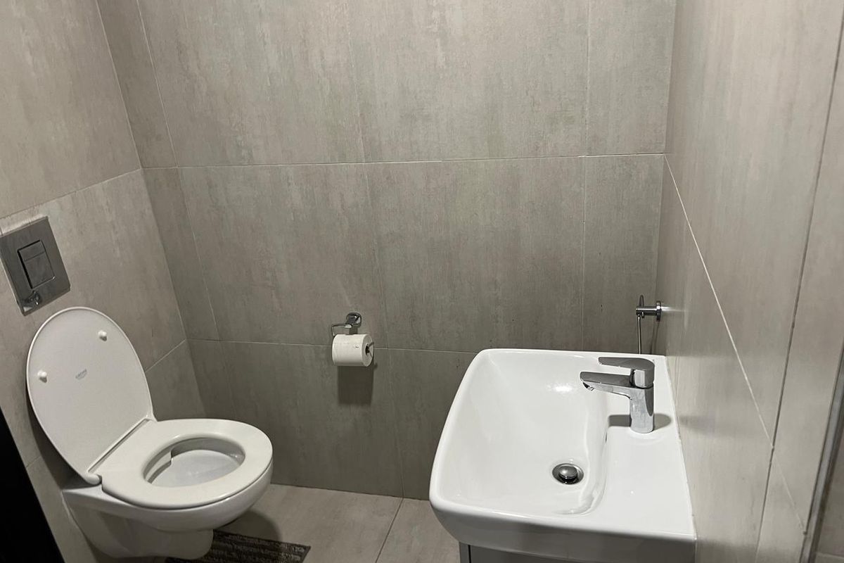 A modern, compact guest bathroom featuring neutral wall tiles, a wall-mounted toilet, and a sleek vanity basin.