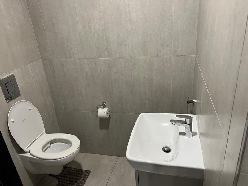 A modern, compact guest bathroom featuring neutral wall tiles, a wall-mounted toilet, and a sleek vanity basin.