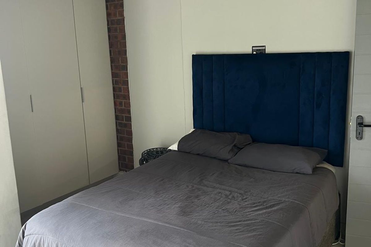 A bedroom featuring built-in wardrobes, a brick accent wall, and tiled flooring.