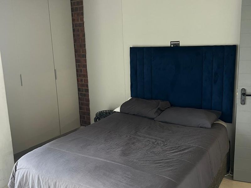 A bedroom featuring built-in wardrobes, a brick accent wall, and tiled flooring.